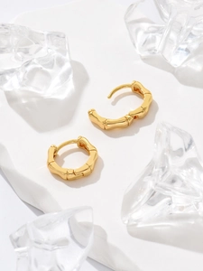 Detailed macro view of gold bamboo texture geometric hoop earrings on a marble surface