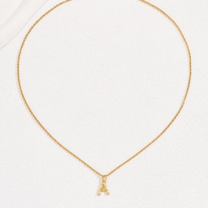 Minimalist gold bamboo style capital letter A pendant necklace on white textured background