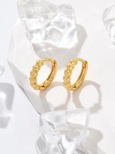 Close-up of gold-plated bamboo heart huggie earrings on a white stone base