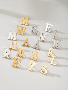 Polished stainless steel letter brooches in gold and silver showing minimalist textures