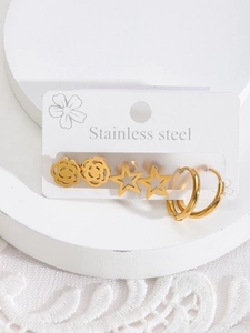 Détail de trois paires de boucles d'oreilles dorées en acier inox : fleur, étoile et anneaux