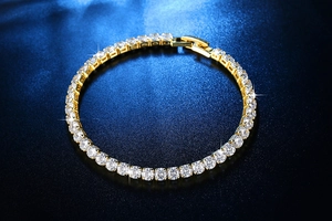 Nahaufnahme eines goldenen Tennisarmbandes mit Zirkonia-Steinen auf dunkelblauem Grund