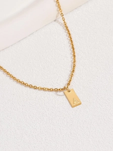 Dettaglio della collana con ciondolo dorato e lettera A incisa su superficie in pietra