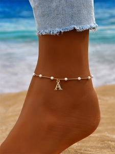 Détail de la chevillère dorée avec perles et lettre A sertie de zircons sur la plage