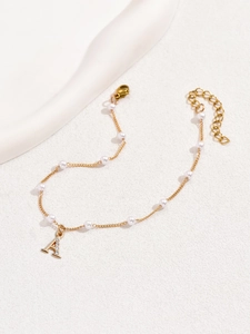 Détail d'une chevillère dorée à perles avec un pendentif lettre A serti de strass