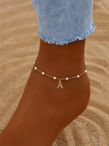 Détail de la chevillère dorée à perles avec pendentif lettre A sur le sable