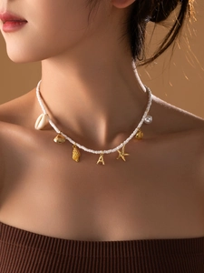 Détail du collier de perles avec breloques dorées et lettre A sur le cou du mannequin