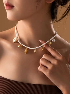 Détail du collier de perles série océan avec breloques dorées en forme de coquillage et A