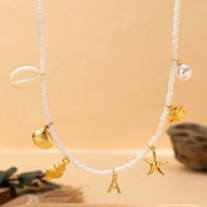 Collier marin avec perles, coquillages dorés et pendentif lettre A sur fond beige