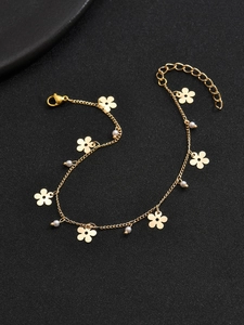 Nahaufnahme eines goldenen Fußkettchens mit kleinen Perlen und Blumen auf schwarzem Grund