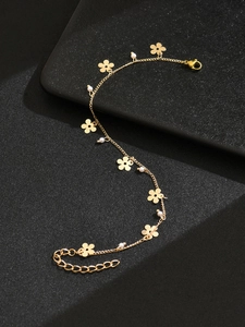 Nahaufnahme der goldenen Fußkette mit zarten Blumenanhängern und runden weißen Perlen
