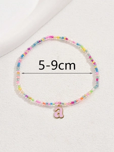 Detalle de una tobillera de cuentas de colores con un colgante de letra 'a' de esmalte rosa