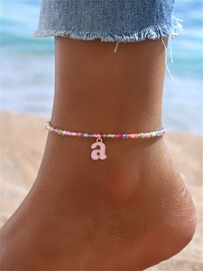 Primer plano de una tobillera de cuentas de colores con colgante de letra rosa en la playa