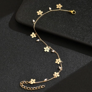 Elegantes goldenes Fußkettchen mit fünfblättrigen Blumen und Perlen auf schwarzem Hintergrund