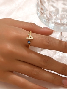 Dettaglio anello dorato regolabile con lettera A in zircone e ciondolo occhio blu