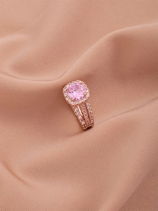 Detail view of pink gemstone engagement ring with three-row pavé band on satin background