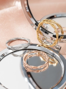 Three-color twisted rings in gold, silver and rose gold shown on mirror reflection