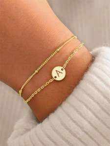 Dettaglio di un bracciale a doppio strato in acciaio inossidabile dorato con ciondolo lettera A