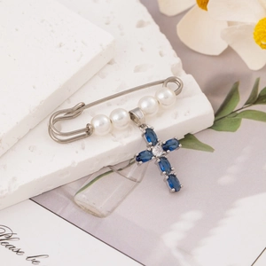 Blue cross pendant pearl safety pin brooch displayed on a natural travertine stone