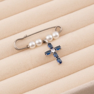 Detail of silver pin brooch with five white pearls and blue cross pendant on beige velvet