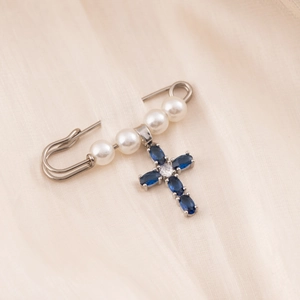 Elegant silver cross brooch with blue crystal pendant and four white pearls on soft fabric