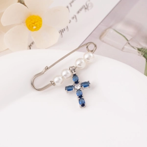 Silver safety pin brooch with white pearls and blue gemstone cross pendant on porcelain