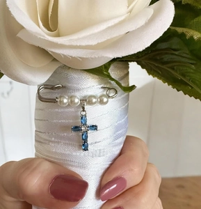 Detail of a blue gemstone cross and pearl safety pin charm on a white wedding bouquet