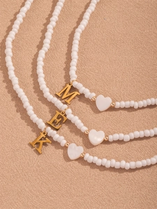 Detailansicht der weißen Perlenkette mit goldenen Buchstabenanhängern und Herzverzierung