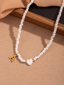 Detailaufnahme einer weißen Perlenkette mit goldenem Buchstaben A und Herzperle