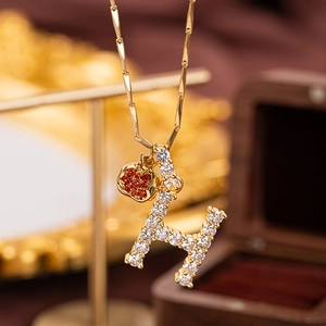 Close-up of golden necklace with crystal letter H pendant and red apple charm