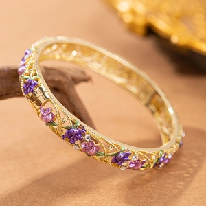 Dettaglio macro di un bracciale dorato vintage con rose in smalto viola e cristalli