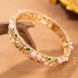 Dettaglio di un bracciale smaltato vintage con perle rosa, strass bianchi e foglie verdi
