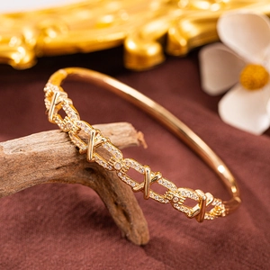 Luxuriöser goldener Kreuz-Armreif mit Zirkonia-Besatz auf dekorativem rustikalem Holz