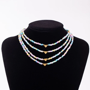 Close-up of four macaron beaded necklaces with gold heart charms on a black neck model