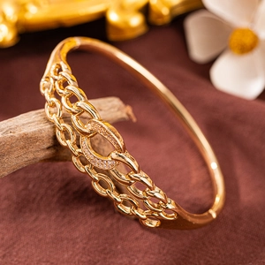 Detailansicht eines vergoldeten Zirkonia-Armreifs mit hohlem Oval-Motiv auf Holz