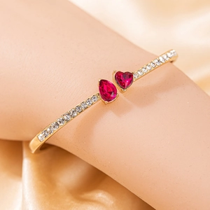 Détail d'un bracelet en or rose avec gemme rouge en cœur et strass brillants