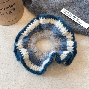 Détail d'un chouchou tricoté main avec des rayures en laine bleues, beige et grises