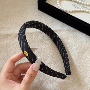 Detail of black twill sponge headband featuring a gold 'Hand Made' metal tag