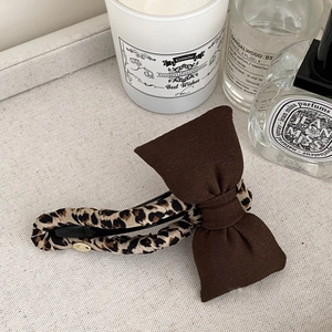 Vintage leopard bow hair clip with dark brown textured fabric and gold logo pendant