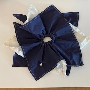 Close-up of dual-layer blue satin and white lace hair scrunchie with silver heart charm