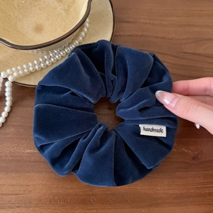 Détail d'un chouchou en velours bleu foncé avec étiquette handmade sur fond bois