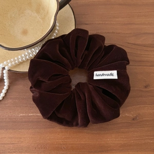 Vue détaillée d'un chouchou en velours marron foncé fait main avec étiquette et texture