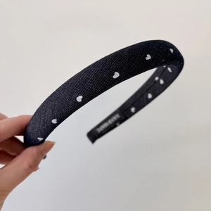 Close-up of handmade black fabric headband with white heart patterns and woven label