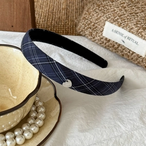 Close-up of navy blue plaid headband with a silver heart charm on white fabric