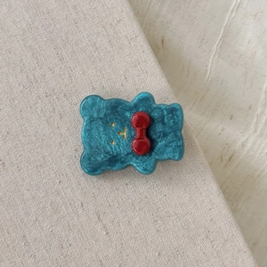 Süße Bären-Haarspange aus blauem Acetat mit roter Schleife auf Leinenhintergrund