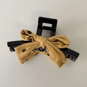 Detail of a black resin hair clip featuring a yellow and brown polka dot fabric bow design