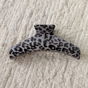 Close-up of a large grey leopard print hair claw clip on a white textured fabric background