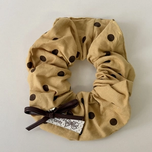 Close-up of yellow polka dot scrunchie with leather bow and candy woven label detail
