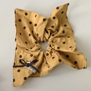 Detail view of yellow polka dot scrunchie with a brown leather bow and fabric label