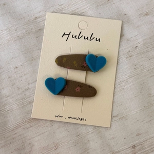Détail de barrettes en velours marron avec cœurs bleus floqués sur une carte de support